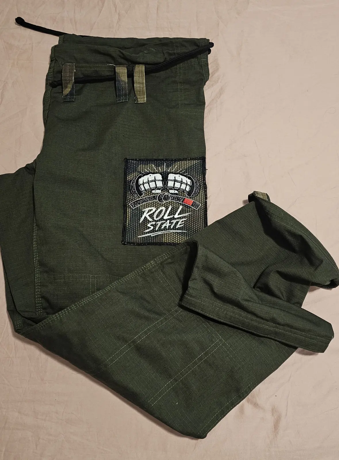 Pantalón real del GI verde militar doblado, con parche Roll State y cordón negro